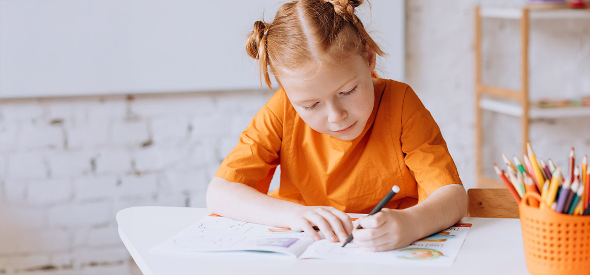 Mädchen mit orangen t-Shirt bei Schreibübungen am Schreibtisch